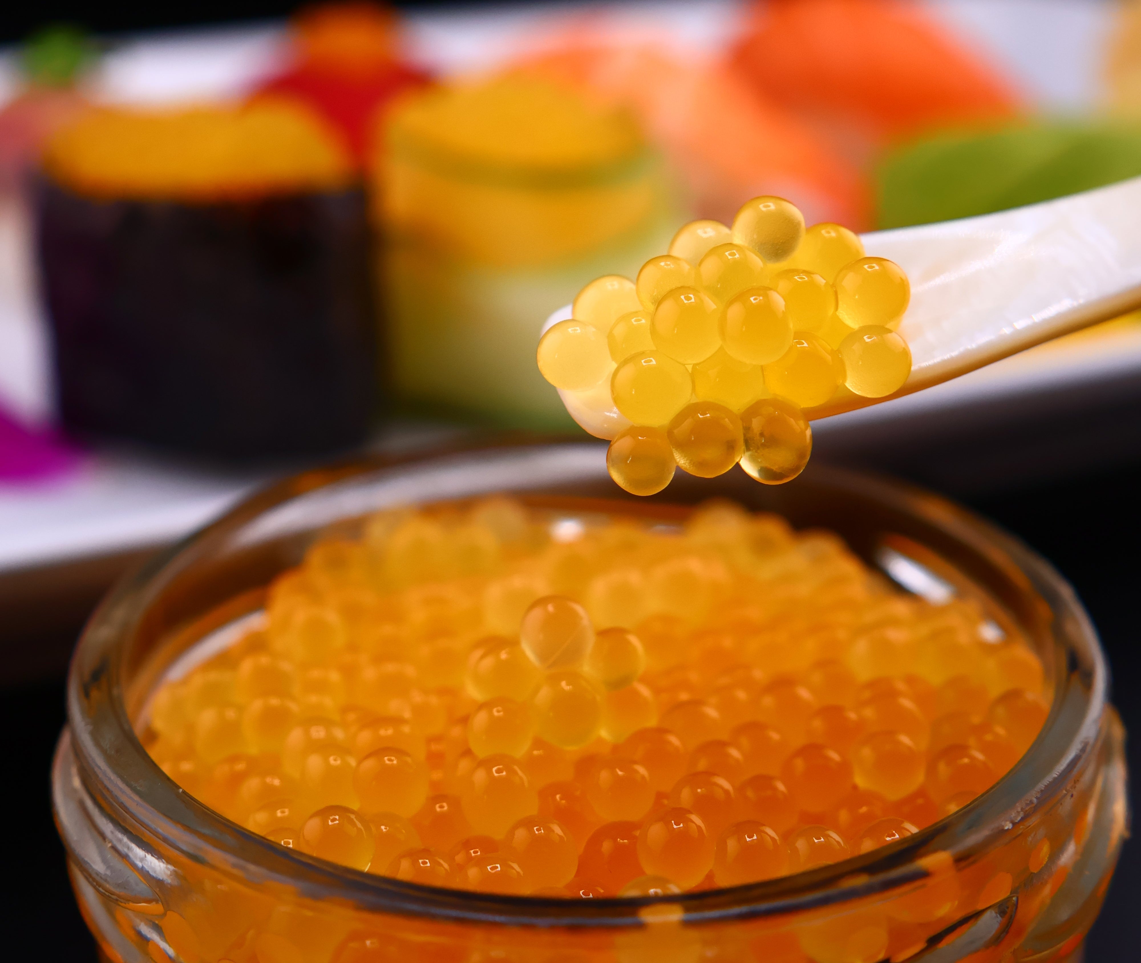 Close-up of a jar of orange caviar, roe with a stick of caviar next to it.