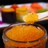 Close-up of a jar of orange caviar, roe with a stick of caviar next to it.