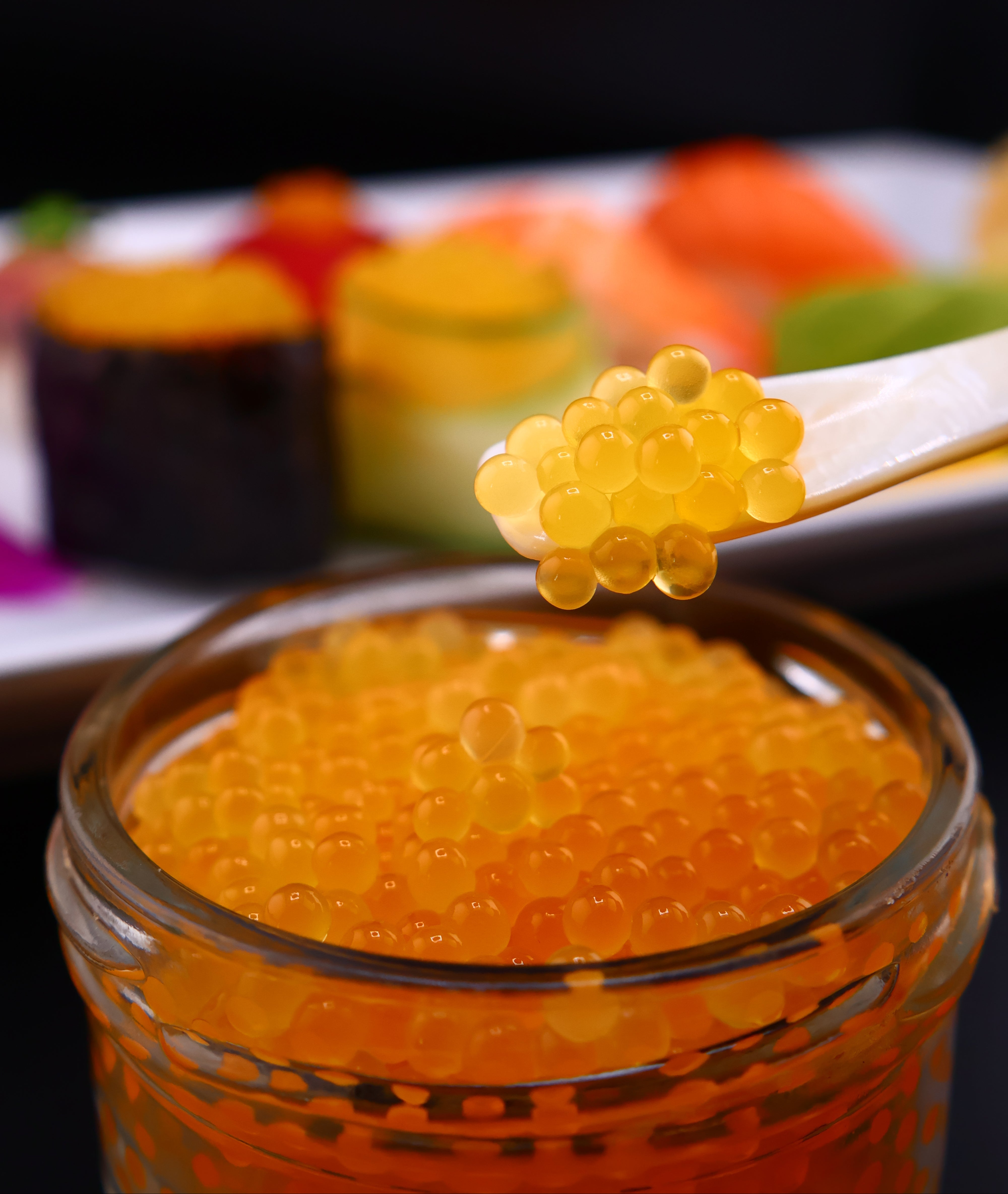 Close-up of a jar of orange caviar, roe with a stick of caviar next to it.