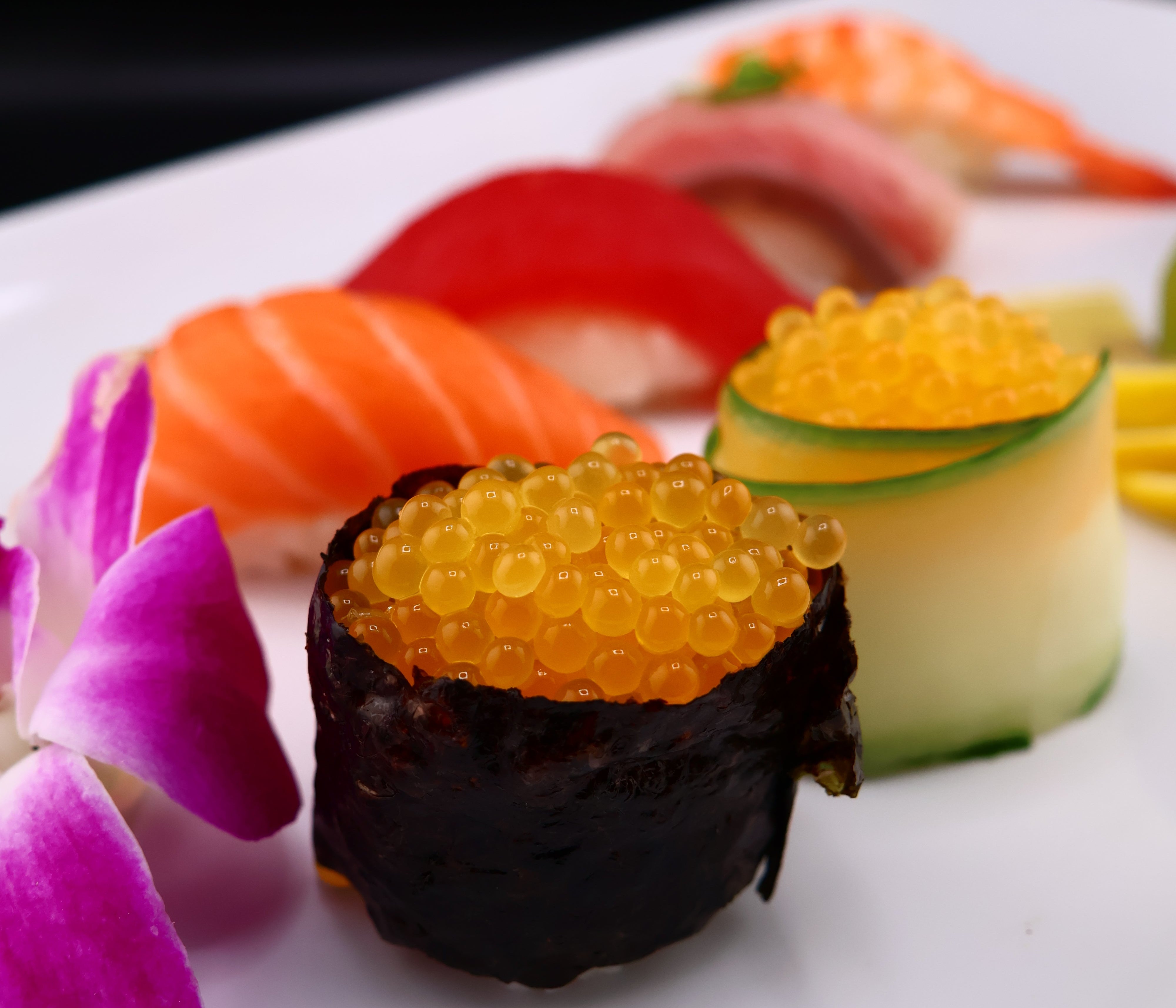 Sushi roll with caviar and vegetables on a white plate with a purple flower.
