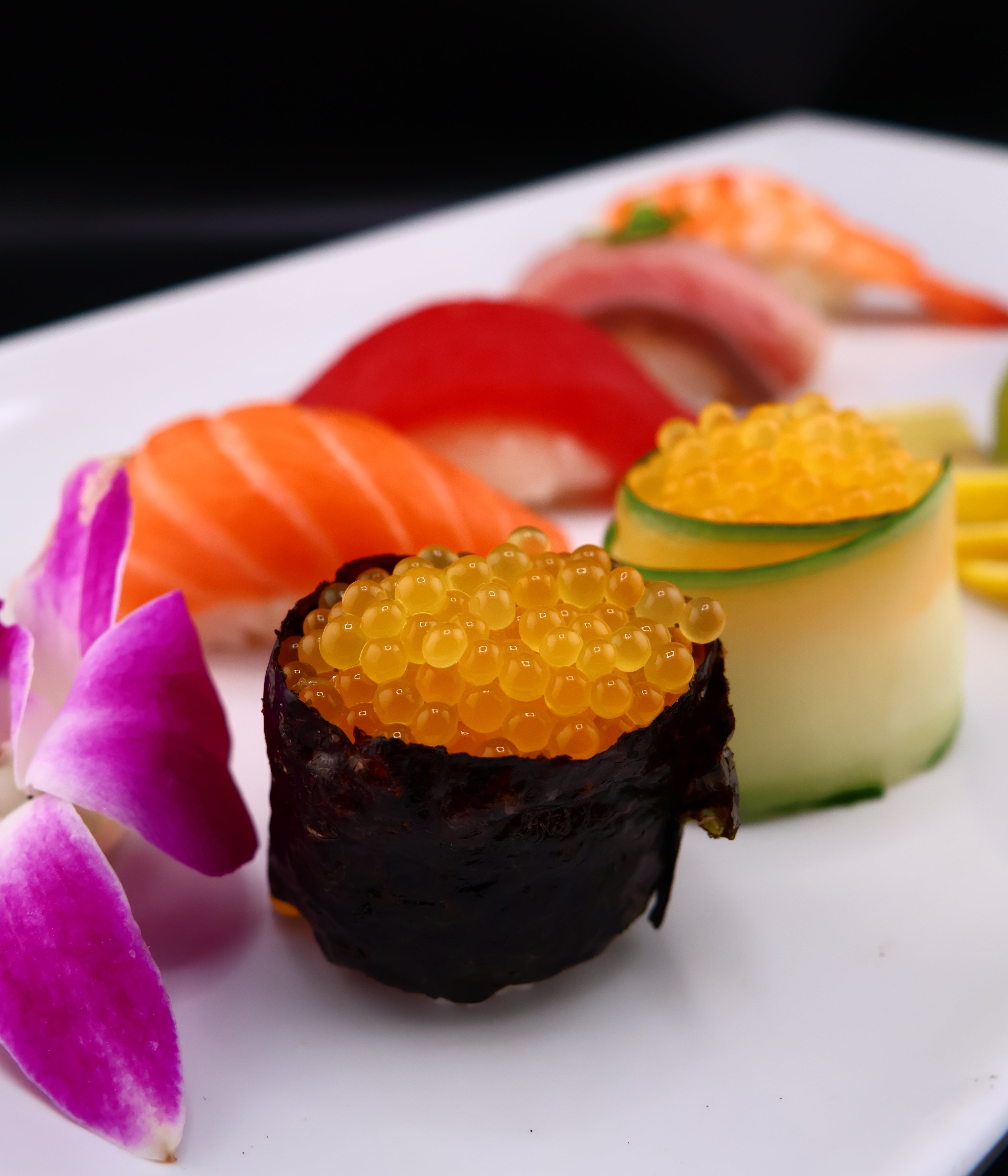 Sushi roll with caviar and vegetables on a white plate with a purple flower.