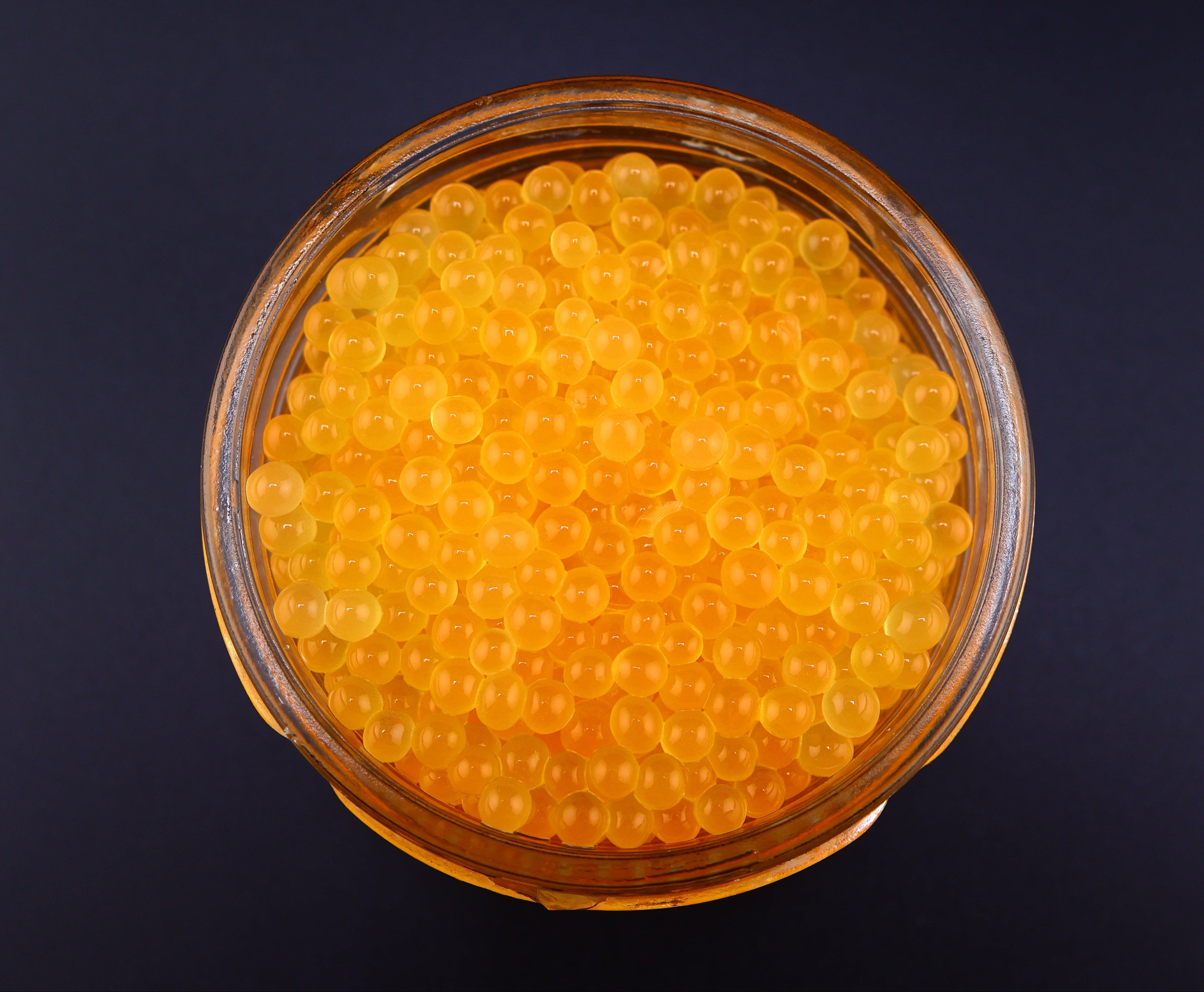 Glass bowl filled with yellow caviar on a black background