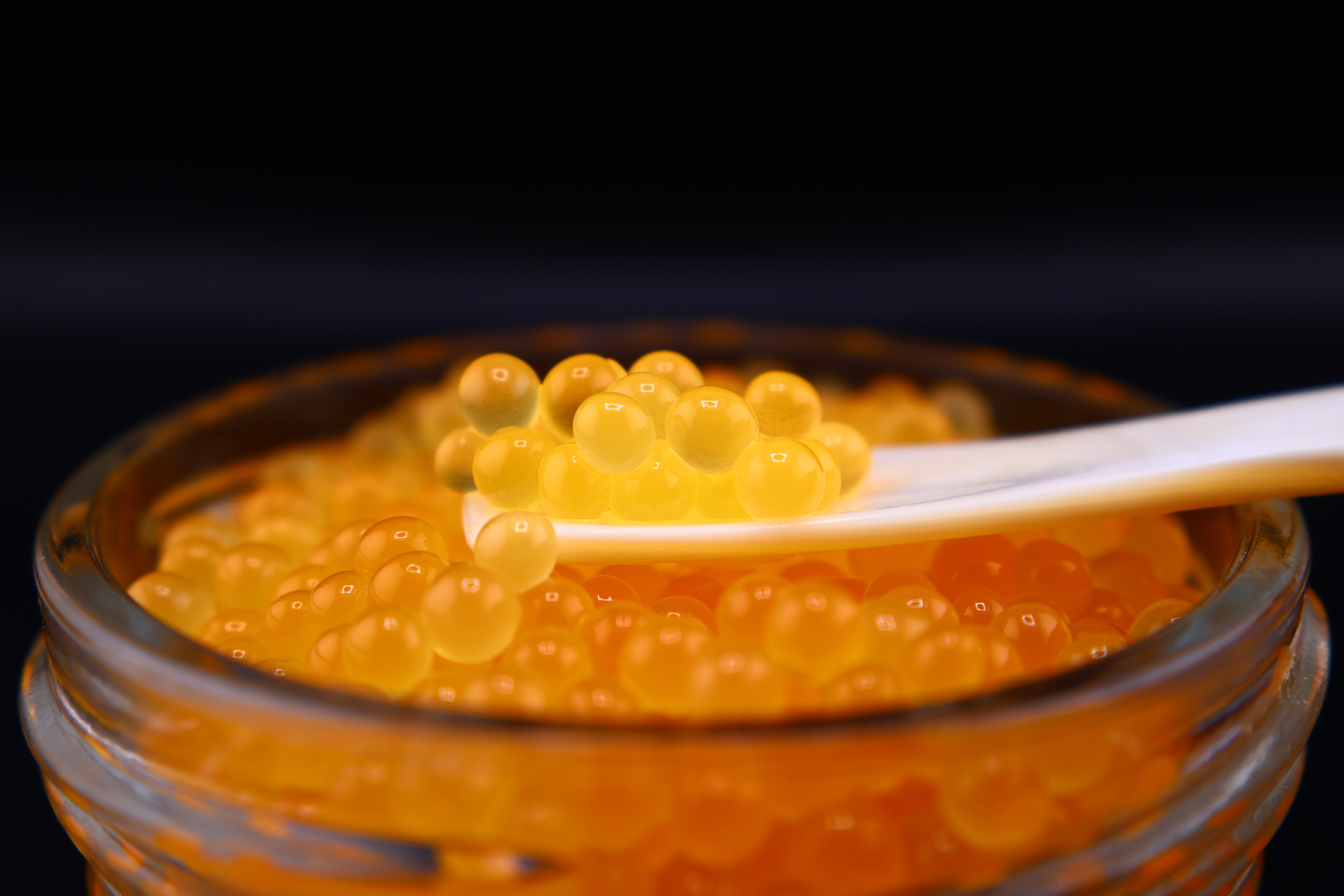 Jar of caviar with a spoonful of caviar on a black background